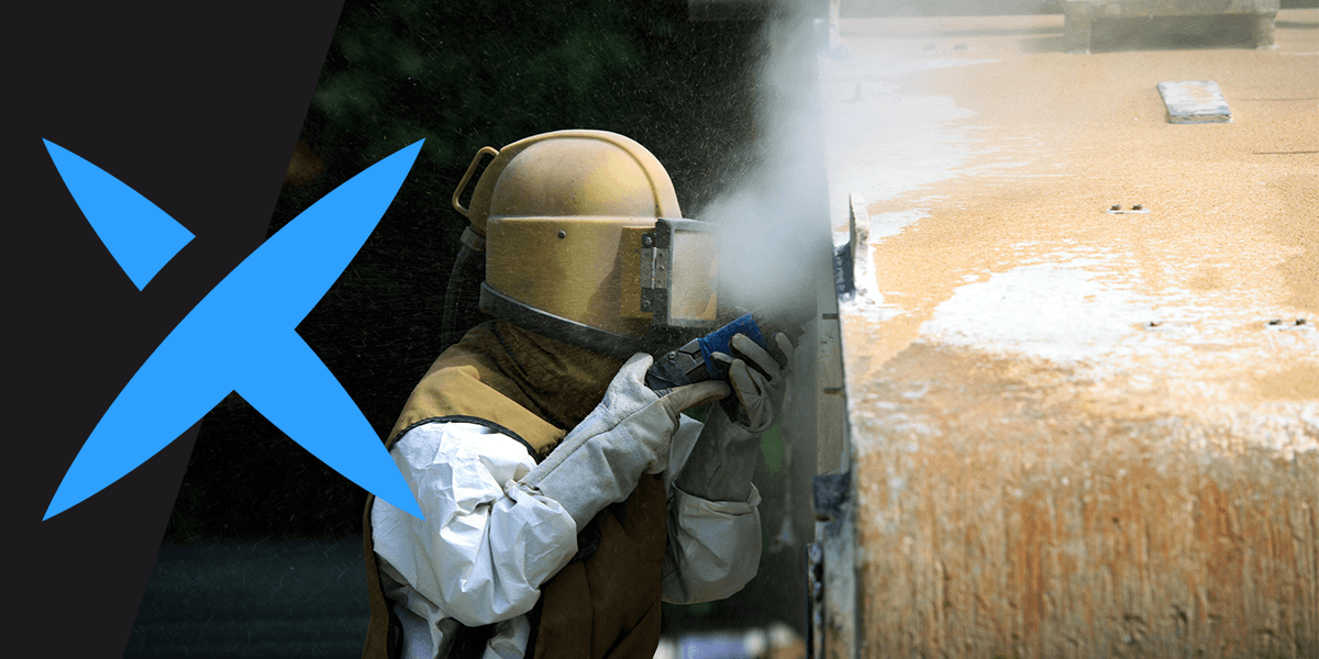 A man in PPE sandblasts a metal tank