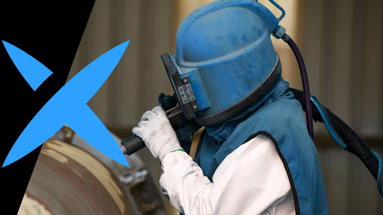 A man in blue PPE sandblasts a pipe