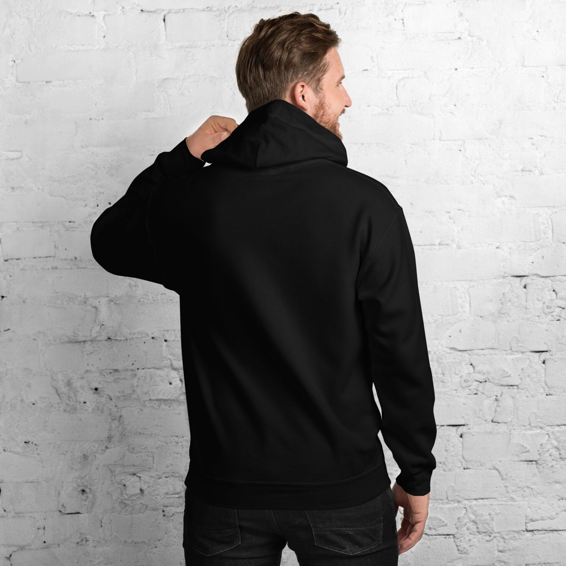 a man wearing a black hoodie is standing in front of a white brick wall