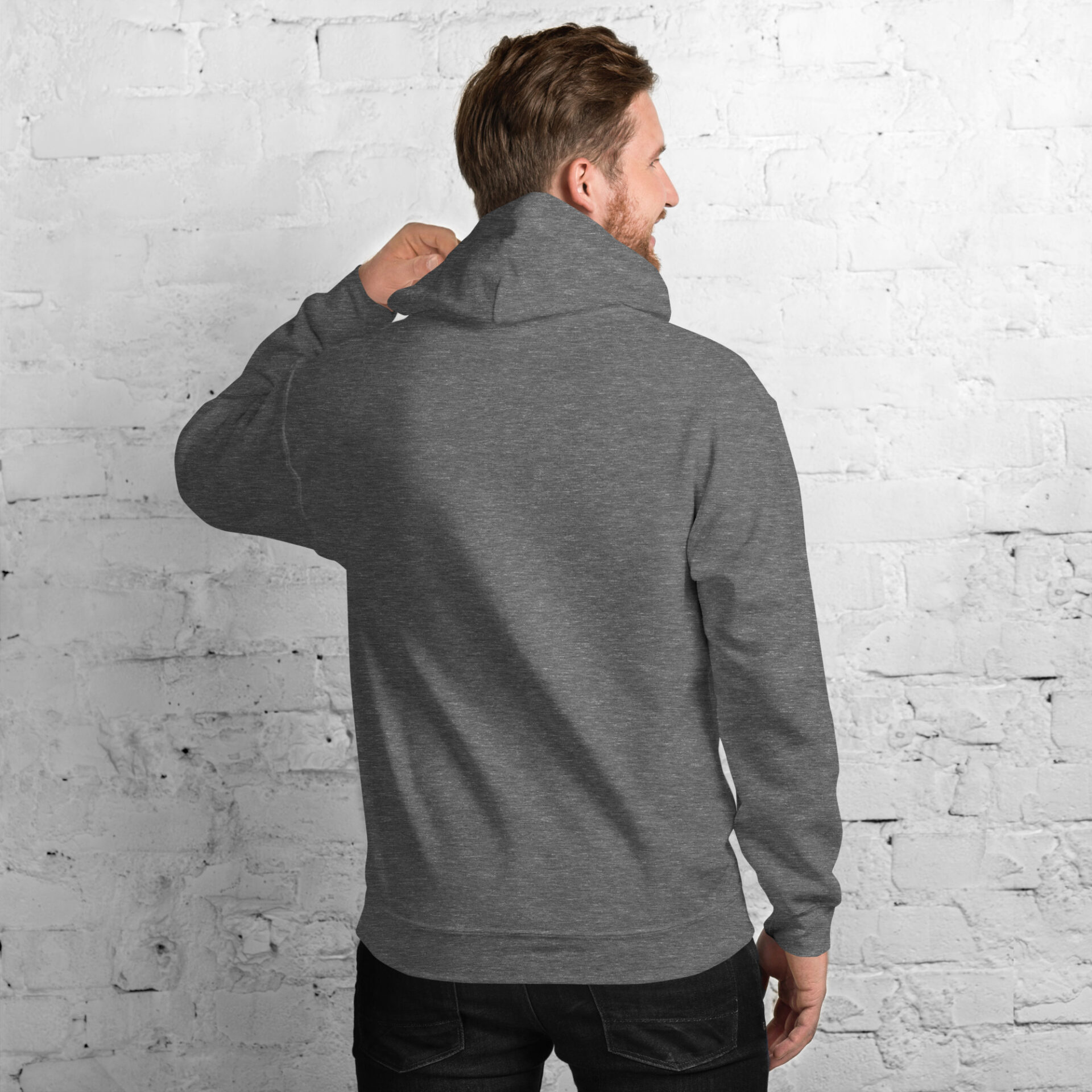 a man wearing a grey hoodie is standing in front of a white brick wall
